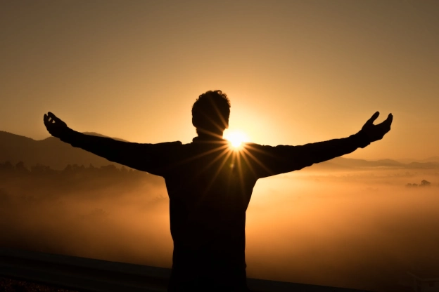 Person standing arms open in sunset