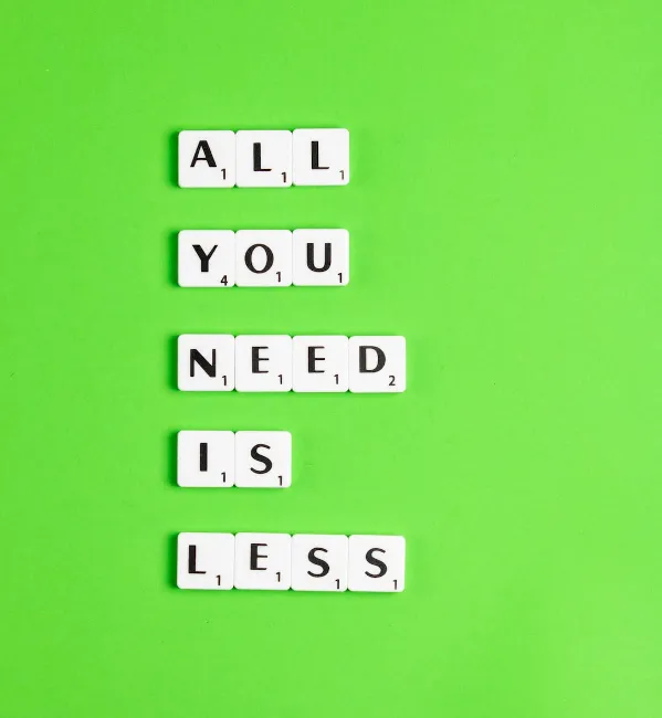 Scrabble tiles on a green background spelling out “All you need is less,” representing minimalist RV living.

