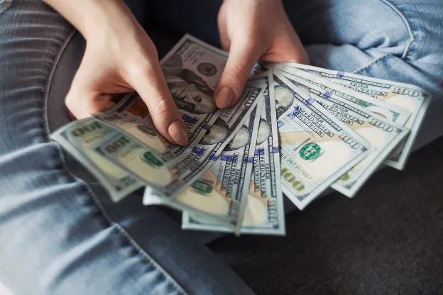  Hands fanning out several currency bills—symbolizing the cost and pricing factors of RV water hoses.

