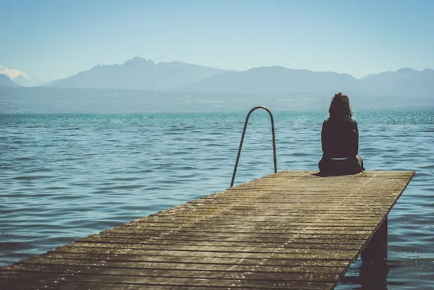 Woman sitting alone at the end of a dock, enjoying peace and solitude—one of the top perks of RV living for beginners.

