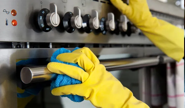  Person wearing yellow gloves wiping a stove clean—visual reminder to clean the RV interior before your first trip.