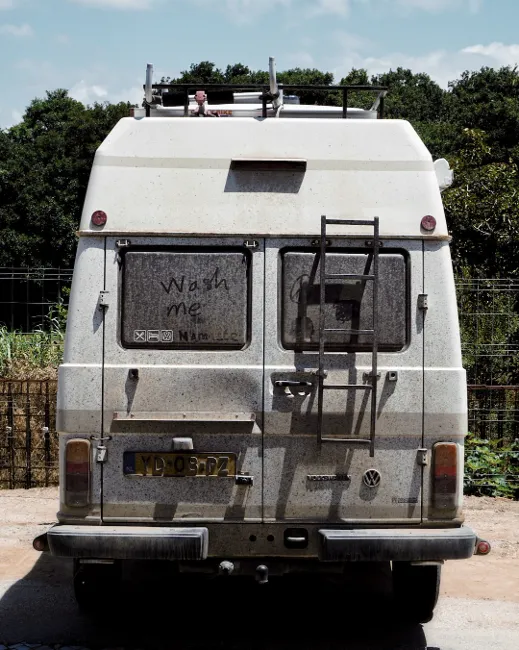 Back of a dirty camper van with “wash me” written in the dust—reminder to wash and inspect your RV during dewinterizing.