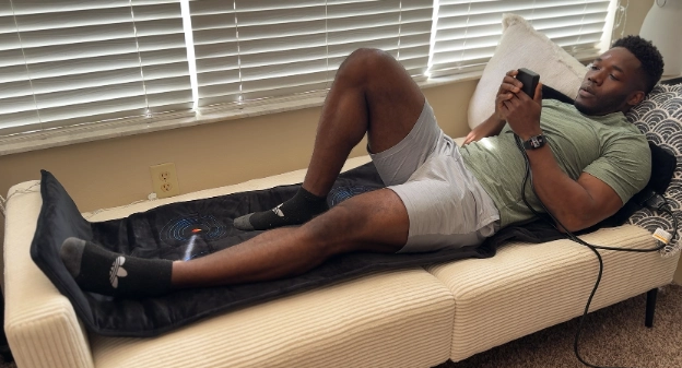 Person using UTK PEMF infrared healing mat at home while adjusting frequency settings