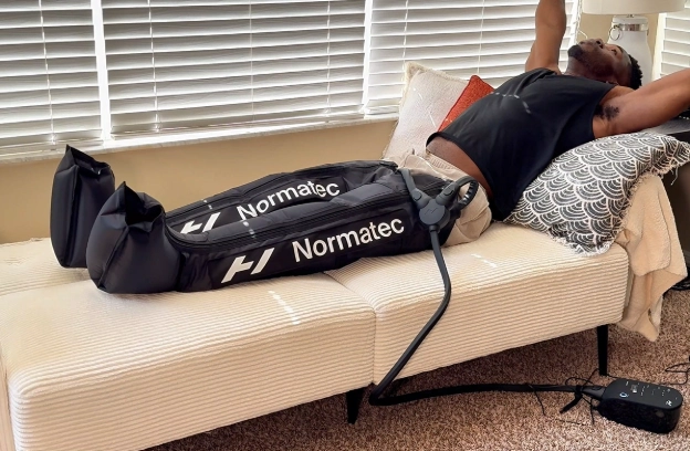 Using Hyperice NormaTec 3 compression boots at home on a couch during a recovery session