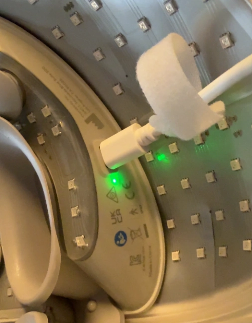 White USB-C charging cable plugged into the side of the TheraFace mask with a green light indicator.