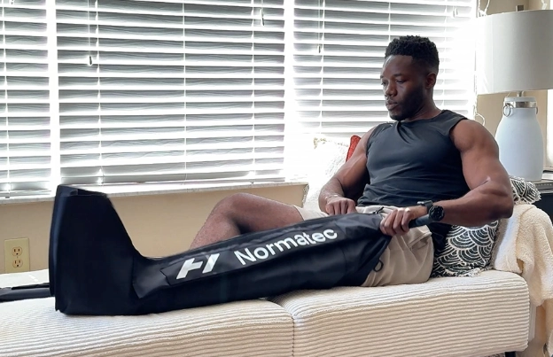 Using Hyperice NormaTec 3 compression boots at home on a couch during a recovery session