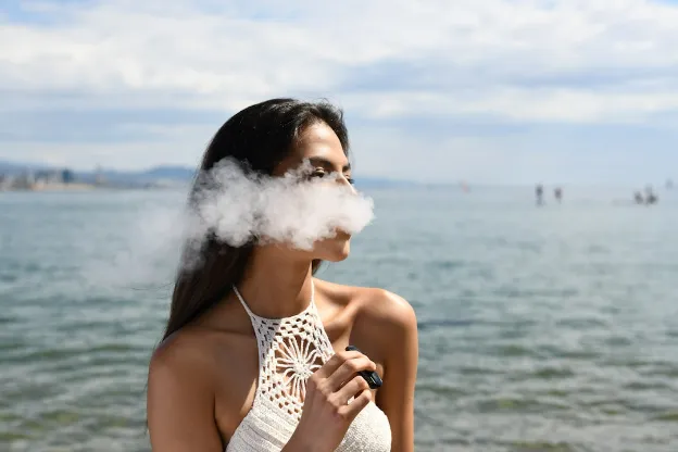 beautiful woman vaping at the seafront in the background