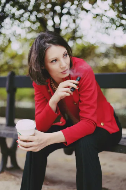 beautiful woman vaping in the park while drinking coffee she is office manager or something