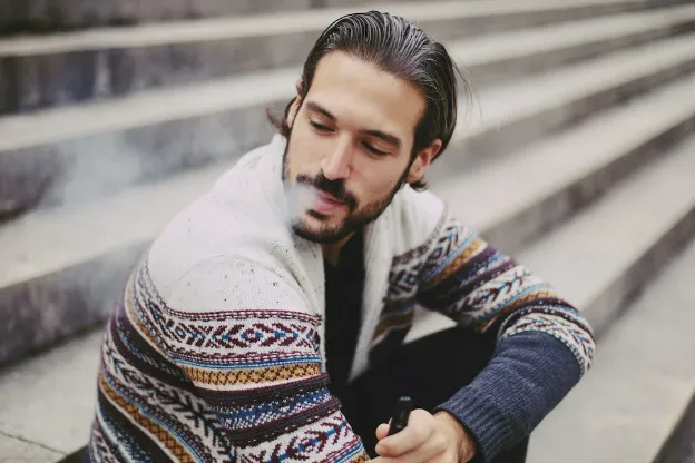 guy in the streat vaping while sitting on the stairs