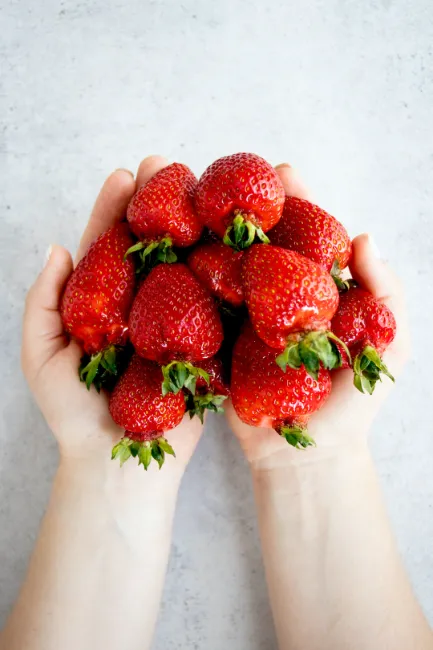 two outstretched hands holding strawberries