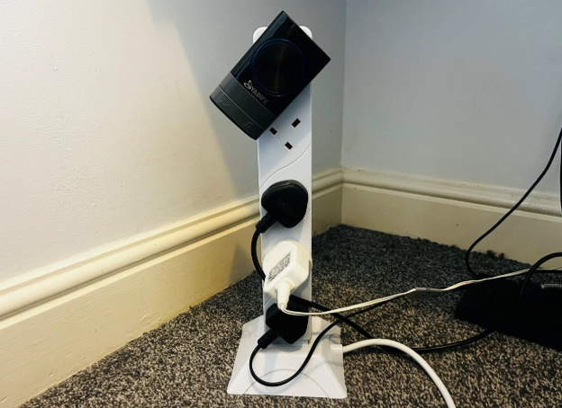 White tower socket extension with multiple plugs on office floor beside desk