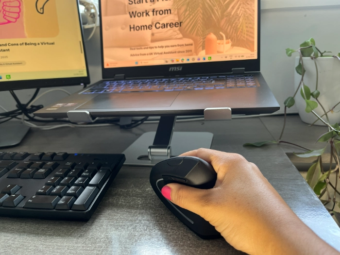 Hand using an Anker vertical ergonomic mouse at a work from home desk with a laptop and monitor.