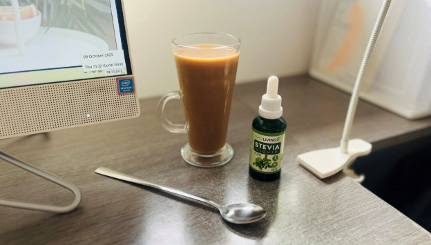 Glass coffee cup with stevia sweetener bottle on desk beside computer in home office setup