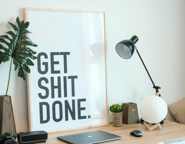 Home office desk with 'Get Shit Done' poster and laptop for Virtual Assistants.