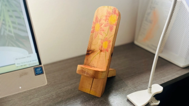 Handmade wooden phone stand with floral design on home office desk beside a white lamp