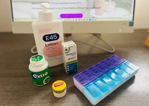 E45 cream, Carmex lip balm, eye drops, vitamins and chewing gum on home office desk