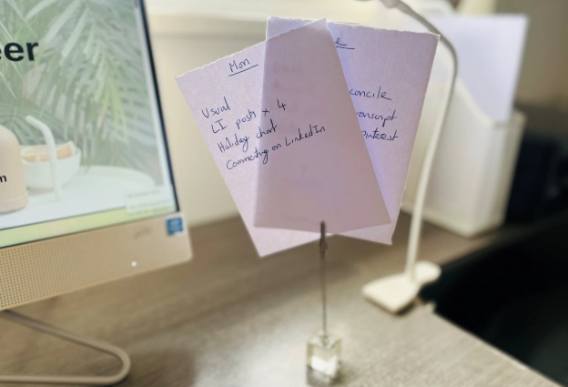 Handwritten desk notes on paper organiser beside computer and lamp in home office setup
