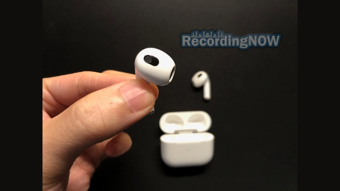 Holding Apple AirPods 3rd generation with MagSafe charging case in background