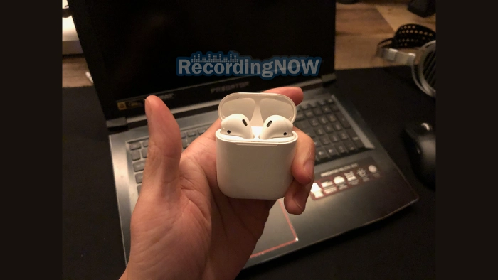 Holding Apple AirPods 2nd generation with Windows Laptop PC in background